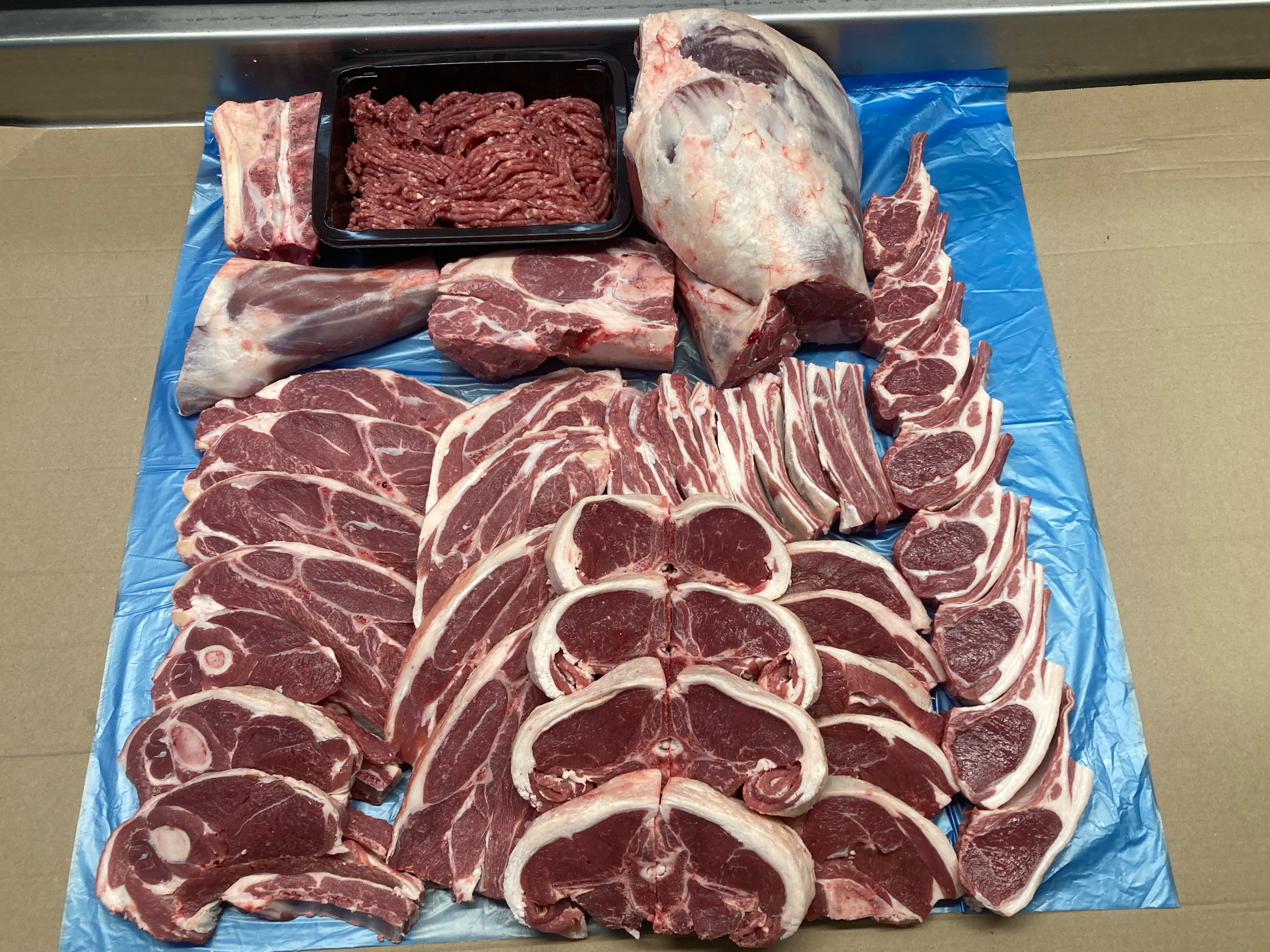 Assorted cuts of raw meat on a blue plastic sheet. Half Lamb