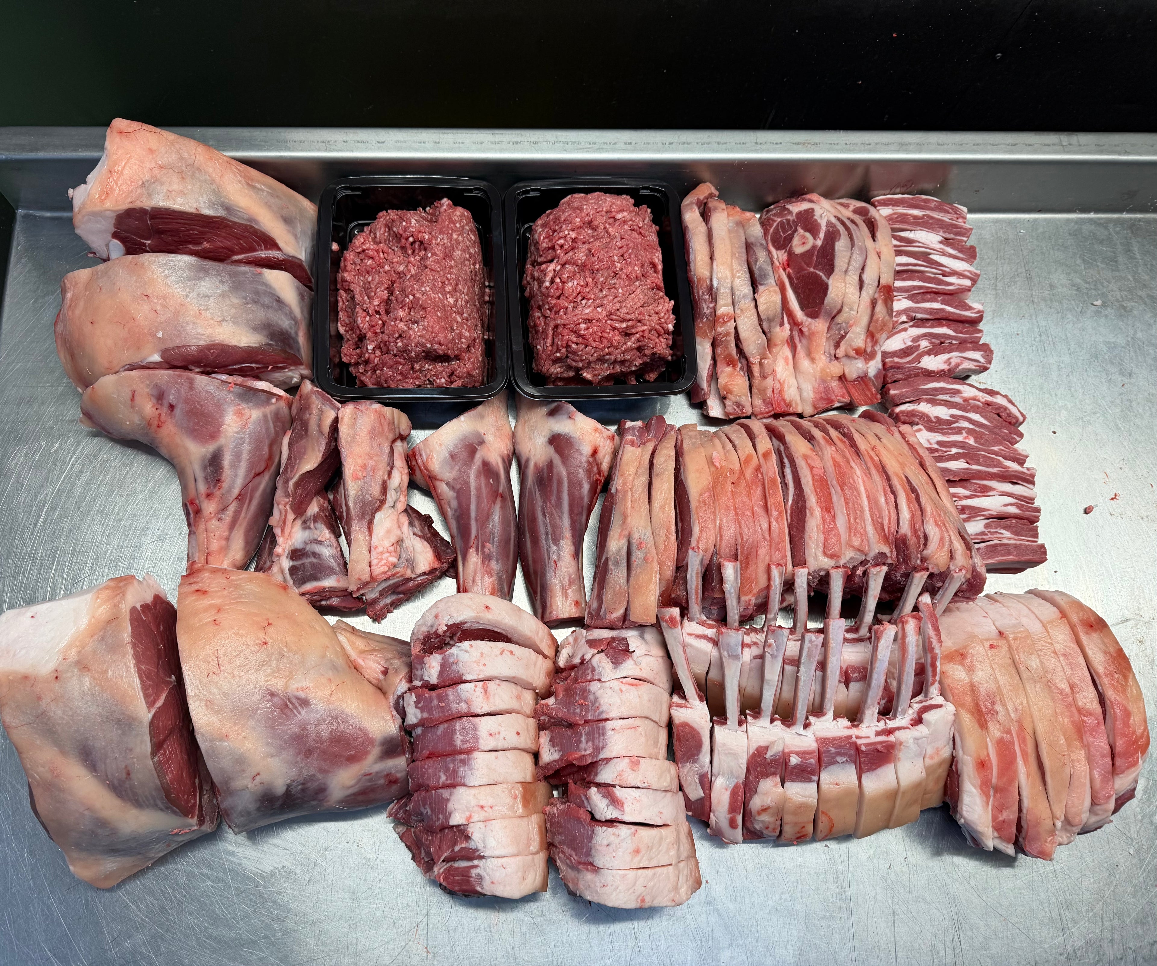 Assorted cuts of raw meat including steaks, chops, and sliced bacon on a metal surface.
