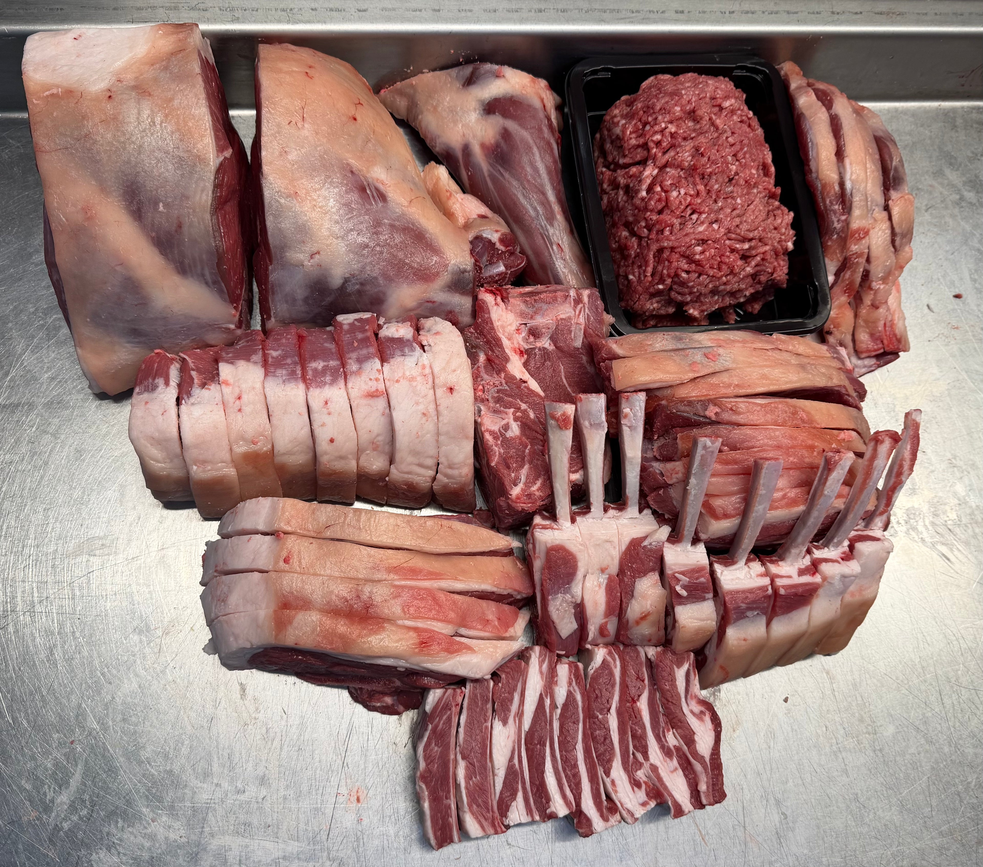 Assorted cuts of raw meat including steaks, ribs, and ground beef on a metallic surface.