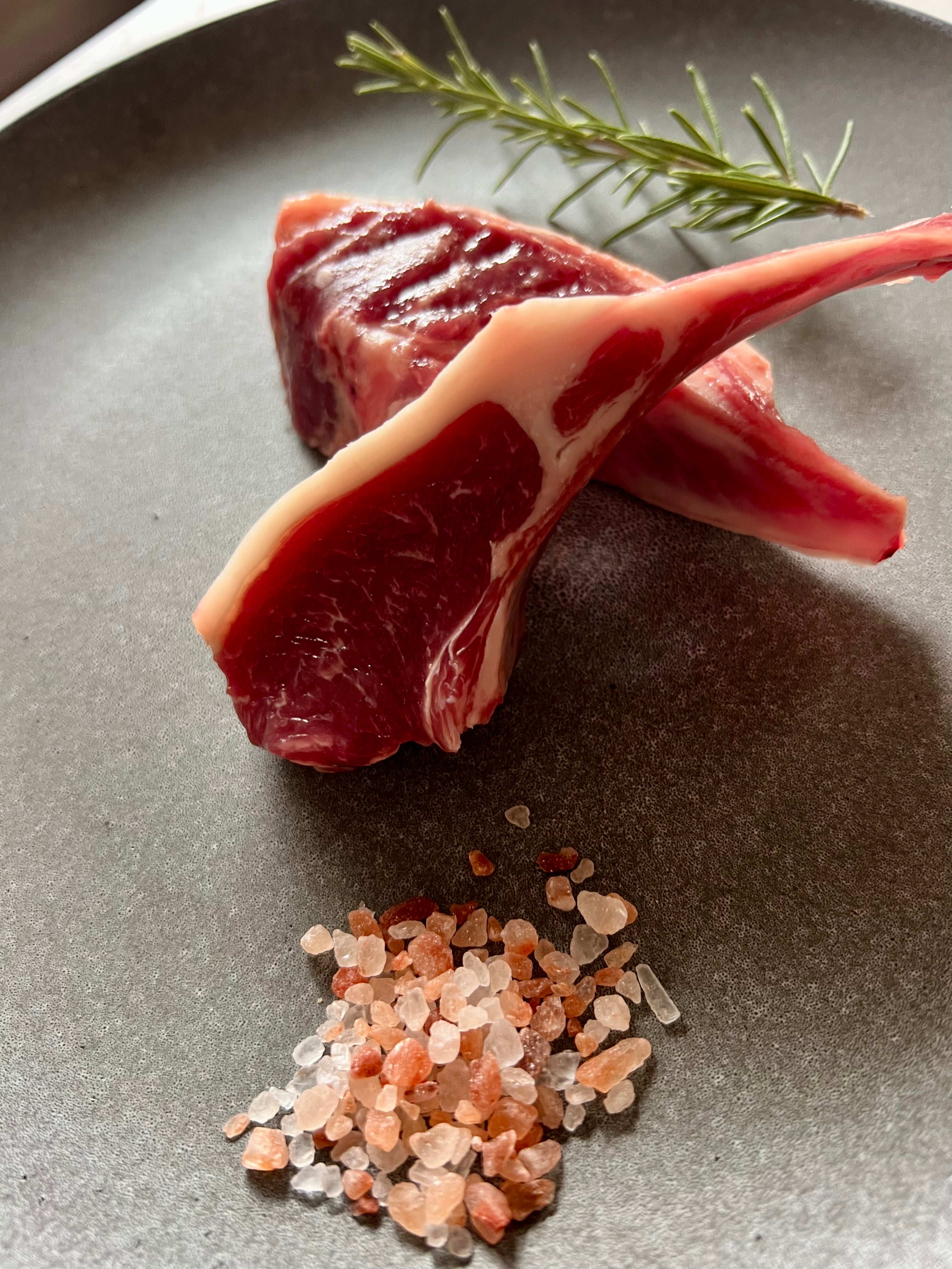 Raw meat with a bone on a plate with pink salt and rosemary.