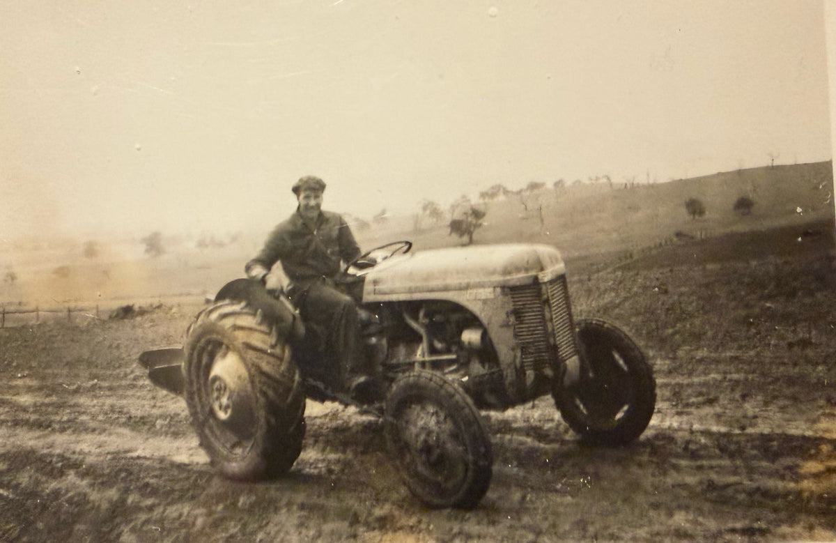 A vintage black and white photograph showing a man driving an old tractor through a muddy field.