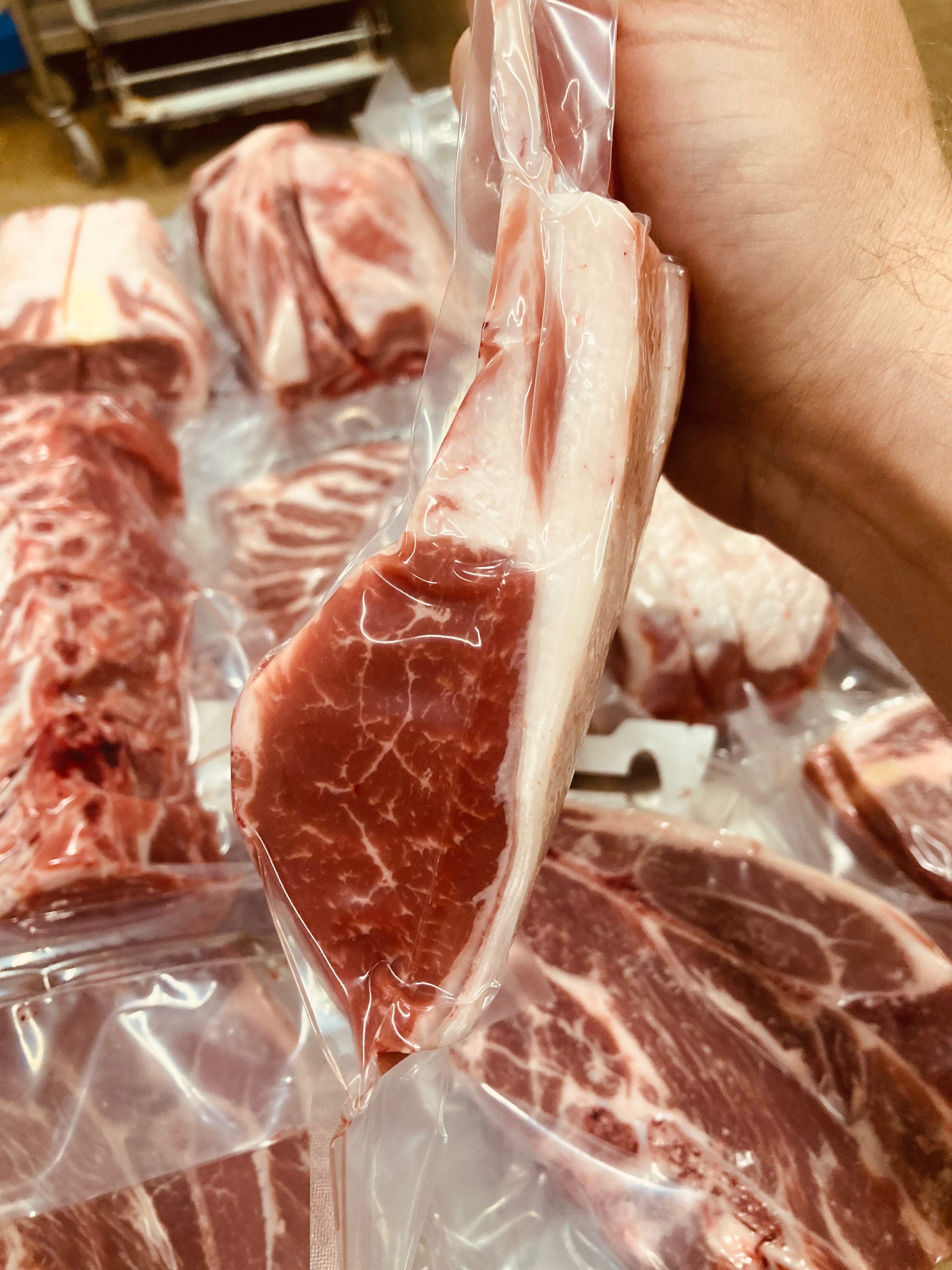 Close-up of raw meat with a hand holding a piece, set against a background of more meat packaging.