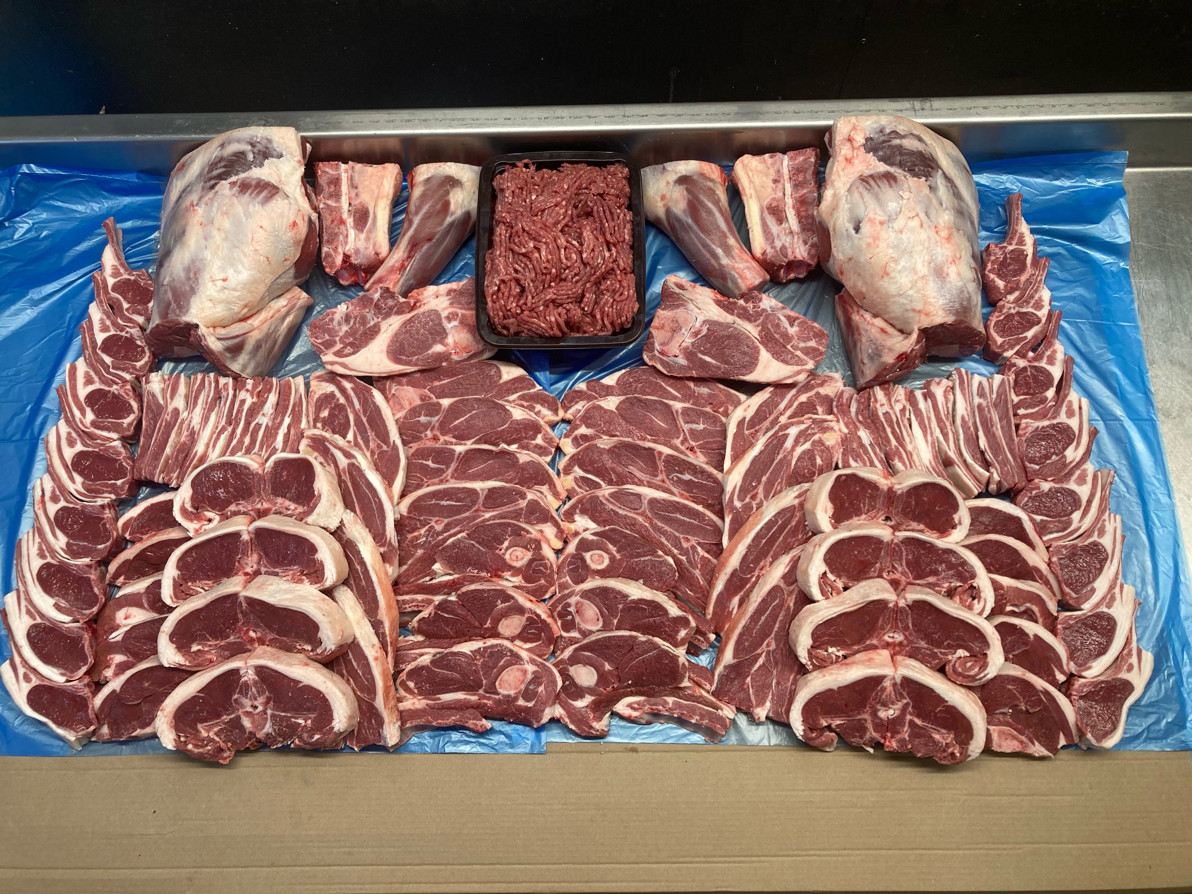 Assorted cuts of raw meat on a blue plastic sheet whole lamb