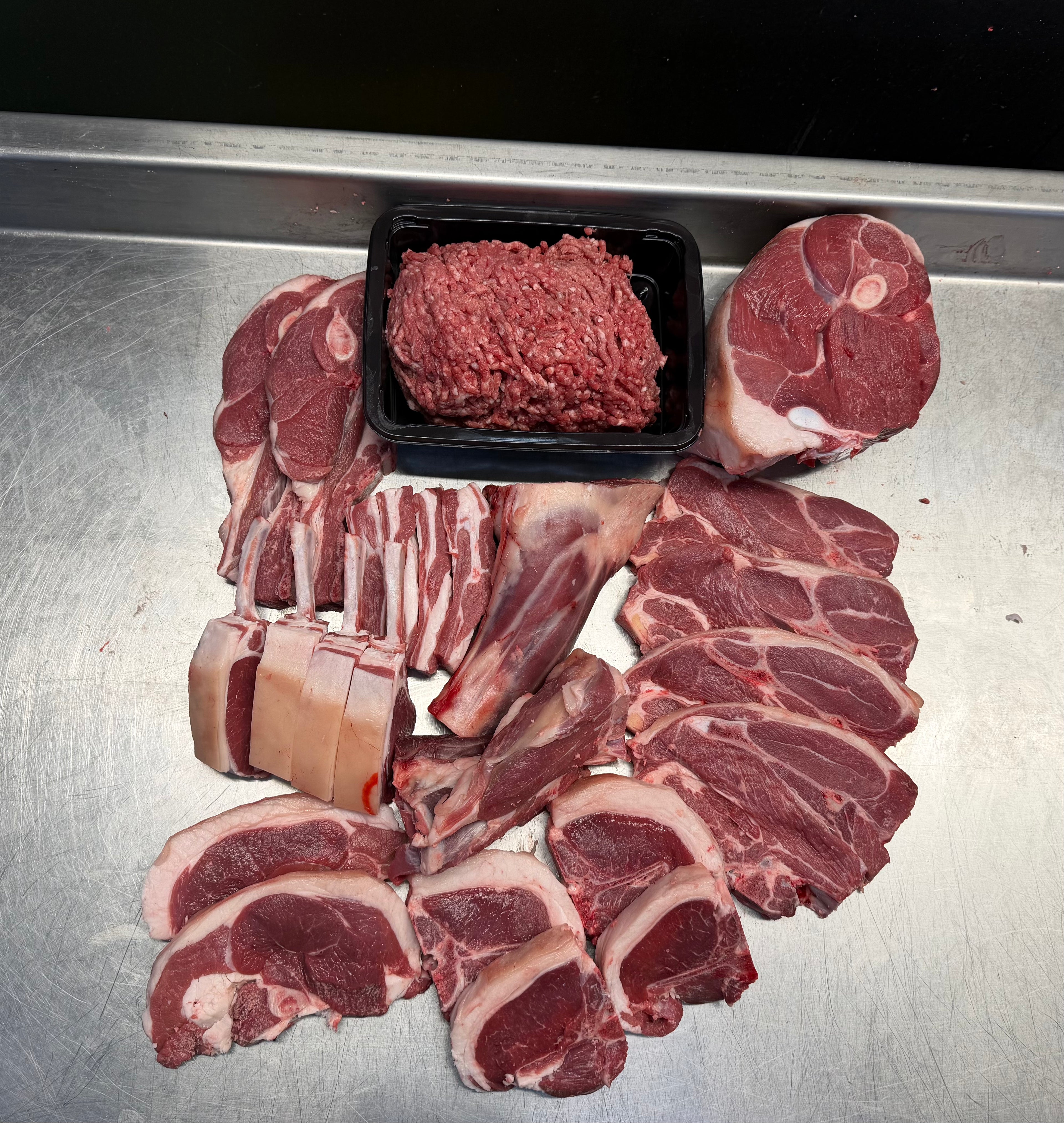 Assorted cuts of raw meat including steaks, chops, and a tray of ground meat on a metallic surface.