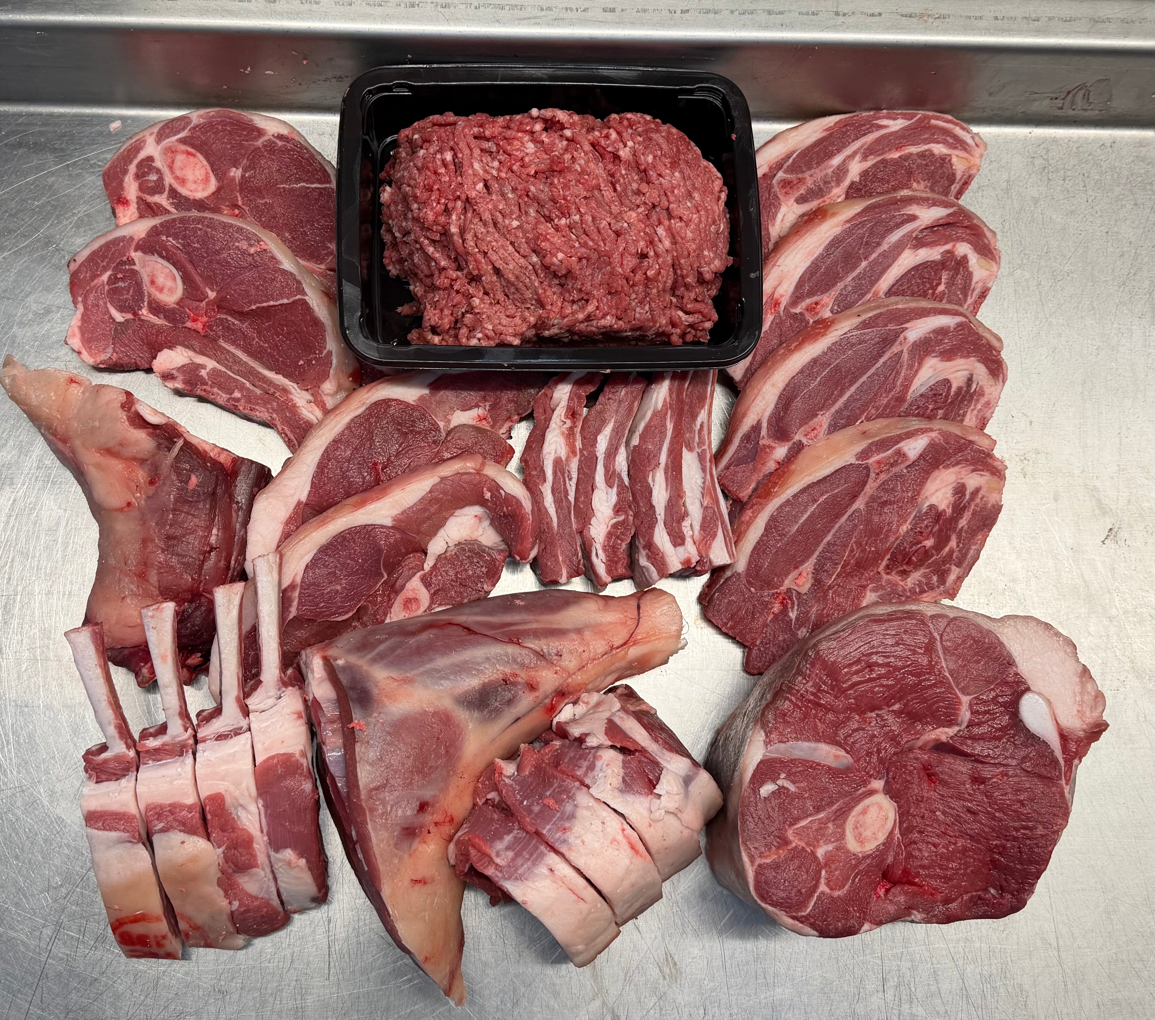 Assorted cuts of raw meat including steaks, chops, and a tray of ground meat on a metallic surface.